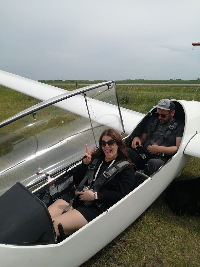 A smiling guest in the front seat of the club's two-seat glider, canopy open, with the pilot in the back seat